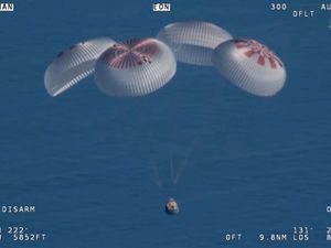 A SpaceX capsule, with main parachutes deployed, floats over the Gulf of Mexico