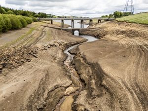 Dry cracked earth exposed at a reservoir with only a small amount of water in a channel at the bottom