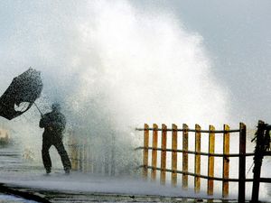 Man with inside umbrella as high waves lap over a harbour wall