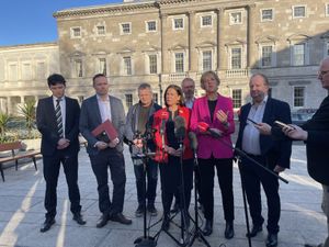 Group of people stand together in front of a microphone. They are holding phones and files.