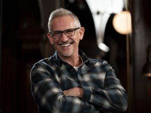 Gary Lineker, wearing a checked shirt and smiling, with his arms folded