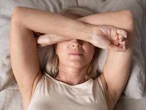 Mature woman laying in bed with arms over face suffering from insomnia
