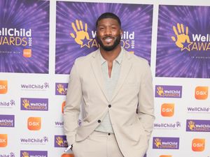 Toby Olubi smiling in front of WellChild Awards signage