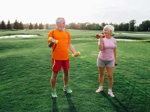 Older man and woman exercise with dumbbells in a park on sunny day