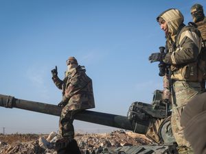 Syrian opposition fighters standing on a seized military armoured vehicle