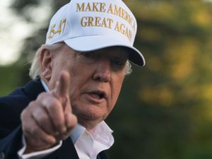 Donald Trump pointing and wearing a white and gold Make America Great Again baseball cap