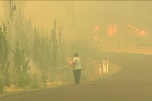In this image made from video taken Dec. 21, 2019, a man sprays water on a fire in Lithgow, New South Wales state, Australia