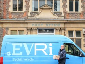 A person stands beside an Evri van holding a parcel