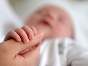 Baby holding onto the thumb of an adult