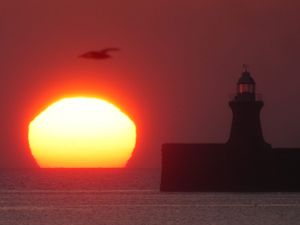 The sun begins to rise behind South Shields lighthouse, on the North East coast.