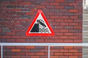 A nearby red triangle sign warning drivers of the dangers of their vehicles toppling into the River Severn at Worcester Rowing Club.