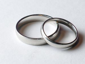 Two silver-coloured weddings rings sit on top of each other on a white table