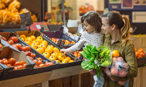 Family in the supermarket. Beautiful young mom and her little daughter smiling and buying food. The concept of healthy eating. Harvest