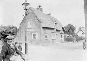 Handwritten on the back of this print is the date 1910 and also: "Old man: Mr Barrow. Boy on corner: Harry Sillitoe. Ernest Burgers, Needle (the handwriting looks like Needle) Chidlow." The sign on the building is "T. Garrett, contractor & builder" and the location is Double Gates in Market Drayton.