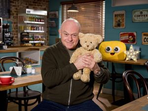 Ross Kemp smiling while holding a teddy, in the EastEnders cafe set