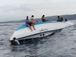 Passengers sitting on a capsized boat in the sea