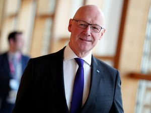 John Swinney walks down a corridor in the Scottish Parliament