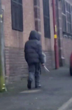 Chilling footage captures the moment a hooded knifeman casually walked down the street while brandishing a huge blade near a primary school. SWNS