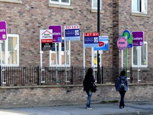 People walk past estate agents' boards outside a block of flats