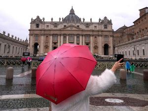 A woman holds a red umbrella as she takes a photo in the rain in St Peter’s Square