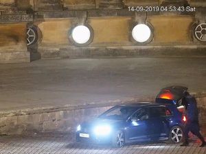 A CCTV image showing three men loading a large object into the boot of the vehicle in the courtyard at Blenheim Palace at nightm Palace