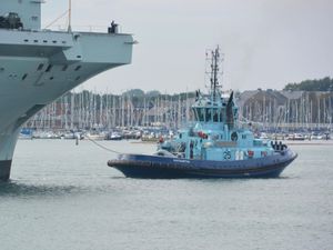 A tug operating in front of an aircraft carrier