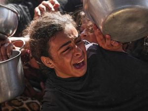 A Palestinian girl struggles to obtain donated food at a community kitchen in Khan Younis
