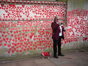 A woman plays the trumpet in front of the Covid Memorial Wall