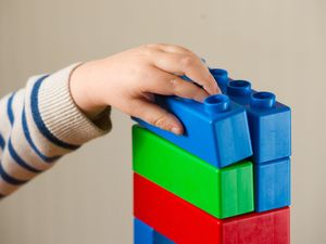 The arm of a child, with their hand on the top of a tower of coloured blocks