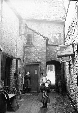 Ludlow. Drew's Court, Ludlow. This picture is used in the book How The Other Half Lived by Derek Beattie of Ludlow. The book caption describes this as Drew's Court just before World War One. 'It was entered by the side of 119 Corve Street that in 1881 was the home of Mary Drew, a dressmaker...' The caption says that the structures on the wall on the right are pigeon coops, and these properties now lie underneath Tesco. The picture is credited in the book to Lottie James