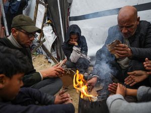 Members of the Abed family warm up by a fire at a tent camp for displaced Palestinians in the Mawasi region, Rafah, southern Gaza Strip