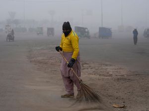 A sweeper cleans as smog envelops the area and reduces visibility in Lahore, Pakistan