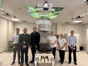 Matty Barnett, Trainee Physicist, Dr Rick Sims, Callum MacMillan, Radiotherapy Engineer, Jayne Matthews, Therapeutic Radiographer, Amanda Welsh, Chief Dosimetrist,and Daniel Kelly, Physicist, with the LINAC Machine and new cameras in the foreground.