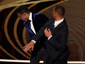 Will Smith, right, hits presenter Chris Rock on stage while presenting the award for best documentary feature at the Oscars 