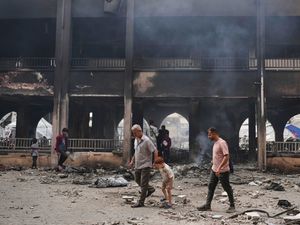 Two men and a child walk in front of a building, blackened and smoking. There is rubble covering the floor.