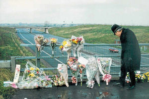 A police officer looks at floral tributes on a motorway bridge after the smash