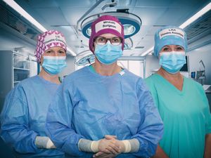 Three medics in caps, scrubs and facemasks in a hospital theatre