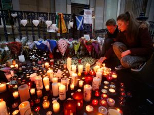 People look at dozens of lit candles on a street