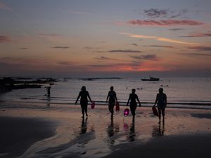 The silhouettes of four swimmers walking from the sea before sunrise