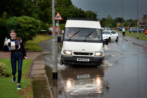 A van mounts the pavement, hidden by water.