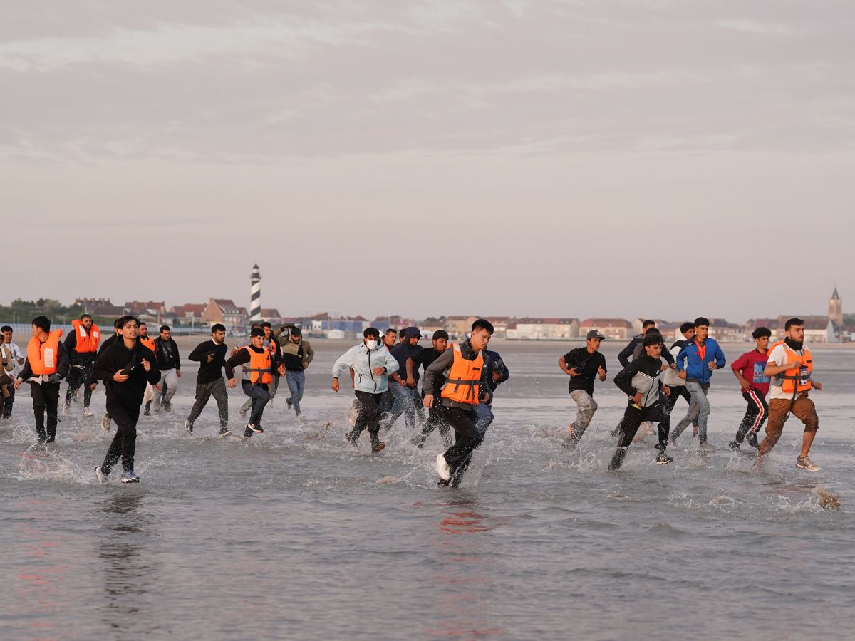 Migrants run across beach to board dinghy in the Channel