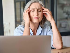 Senior woman with grey hair looking stressed and massaging her head