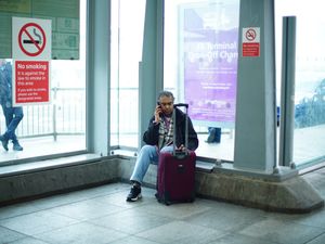 A passenger sitting next to their suitcase, talking on their phone