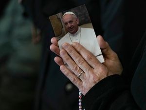 Nun's hands holding rosary beads and a picture of Pope Francis