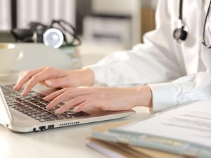 Close-up of female doctor typing on laptop sitting at a desk