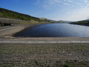 A view of low water levels at Woodhead Reservoir in Derbyshire, under a blue sky