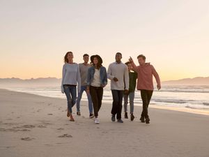 A group of people walking on a beach at sunset