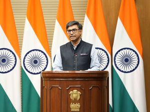 Vikram Misri speaking from a podium, with several Indian flags behind him