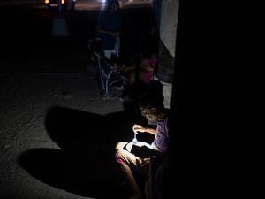 A woman illuminates her plate of food with her phone’s flashlight on a street during a general blackout in Havana