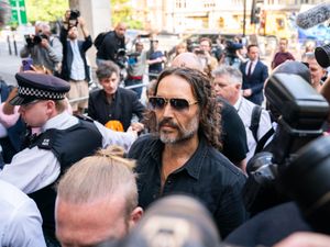 Russell Brand surrounded by people and wearing sunglasses